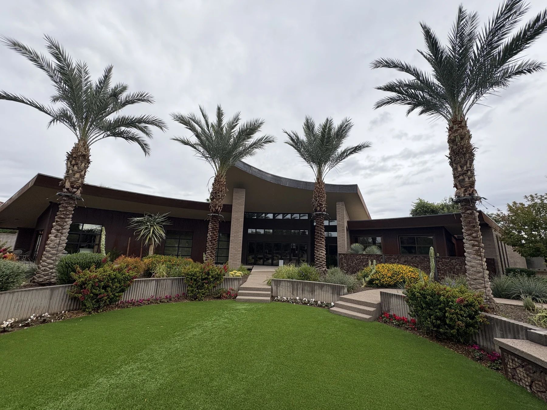 Tall palms framing an estate garden with lawn, flowering beds, and layered desert planting